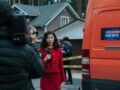 Female reporter in red with microphone reporting live at an outdoor crime scene with a news van.