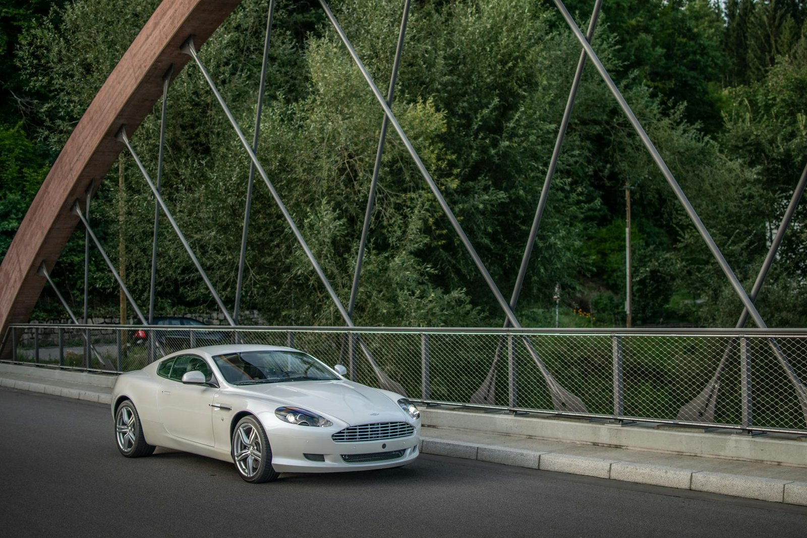 A sleek white sports car parked on an elegant bridge surrounded by lush green trees.