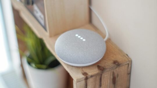 A Google Home Mini smart speaker on a wooden shelf, blending technology with home decor.