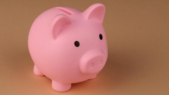 A pink piggy bank symbolizes savings and budgeting on a simple brown backdrop.