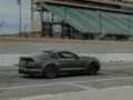 A dark sports car driving on an empty race track next to grandstands.