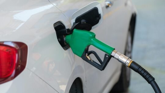 Close-up of a green nozzle refueling a white car at a gas station.