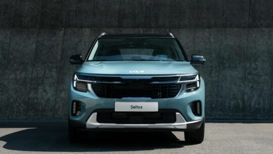 A modern blue Kia Seltos SUV parked against a concrete wall in daylight.