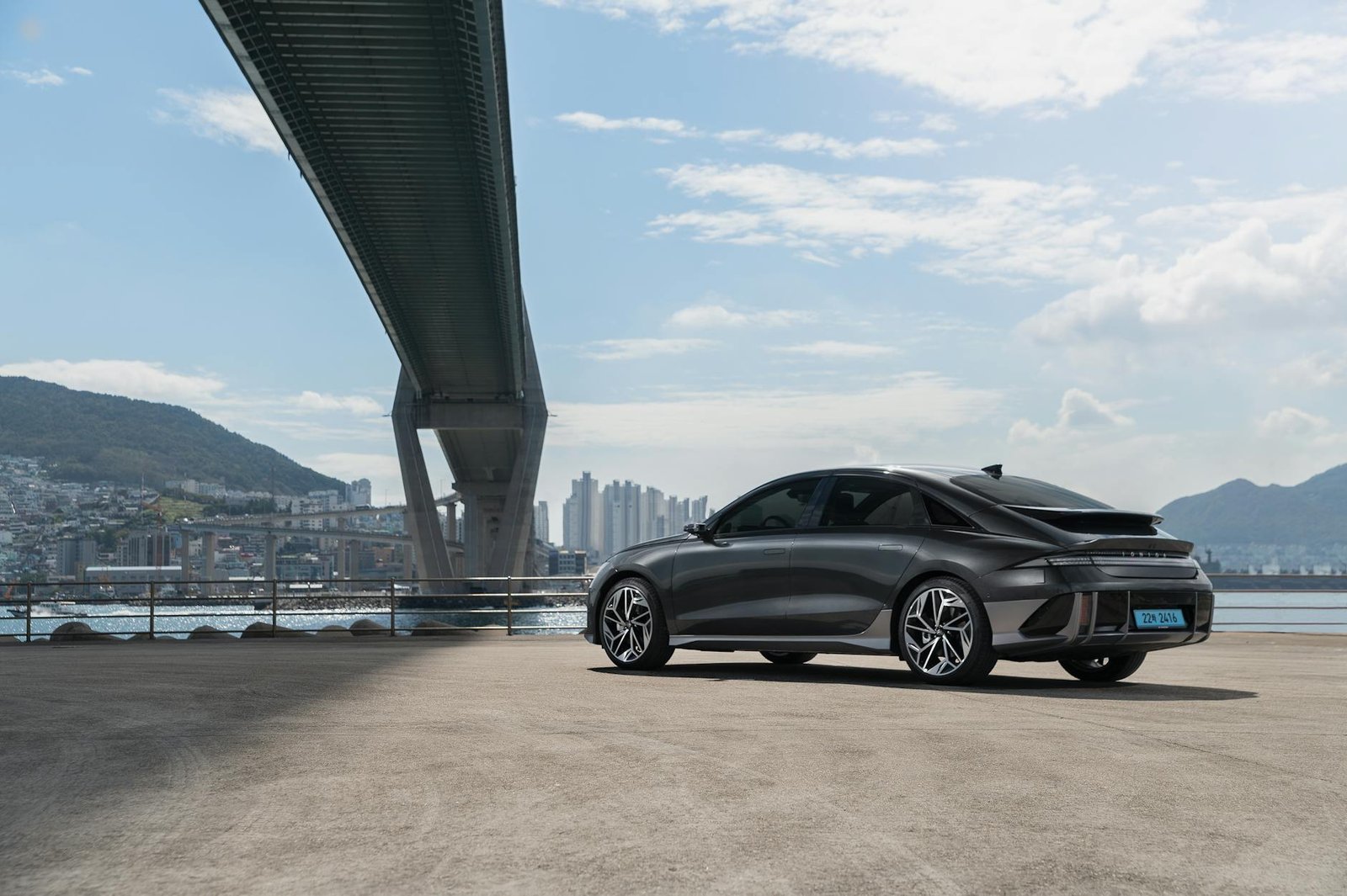 Sleek electric Hyundai car parked under a modern bridge in Busan, South Korea.