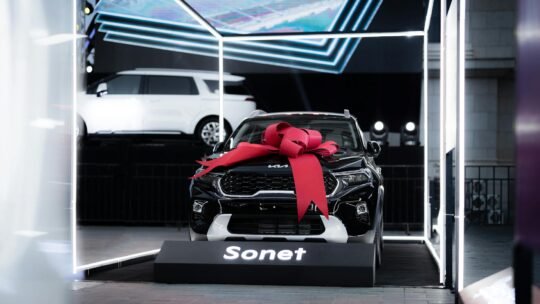 A black Kia Sonet with a red bow on display indoors, highlighting luxury and modern design.