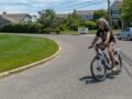 A man enjoying a ride on an electric bicycle in a sunny suburban street in Patchogue, NY.
