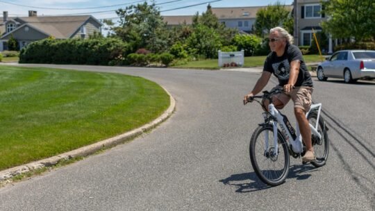A man enjoying a ride on an electric bicycle in a sunny suburban street in Patchogue, NY.