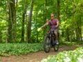 A man riding an electric bike on a forest trail during summer.