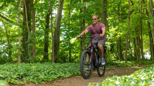 A man riding an electric bike on a forest trail during summer.