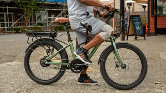 A man leisurely rides an electric bicycle on a city street, enjoying the outdoors.