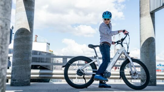 A cyclist rides an electric bike in an urban setting under a blue sky.