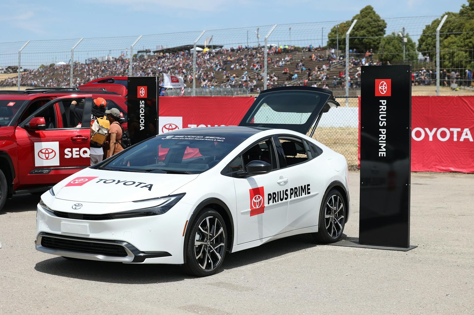 A Toyota Prius Prime on display at an outdoor car exhibition with spectators in the background.