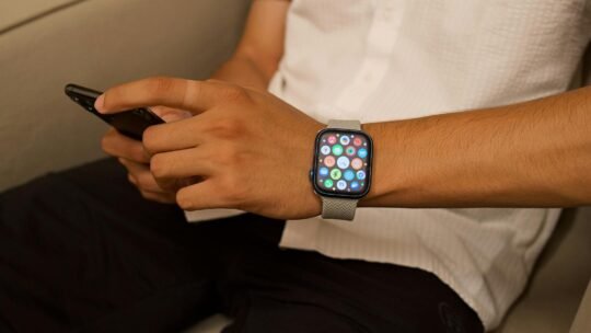 A person sitting indoors, interacting with a smartphone and smartwatch.