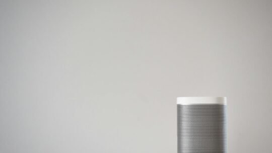 A sleek, wireless smart speaker on a wooden table against a plain wall.