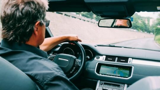 A man driving a convertible car on a scenic highway with a focus on the dashboard.