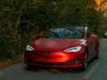 Sleek red electric car driving through a scenic forest road on an autumn day.