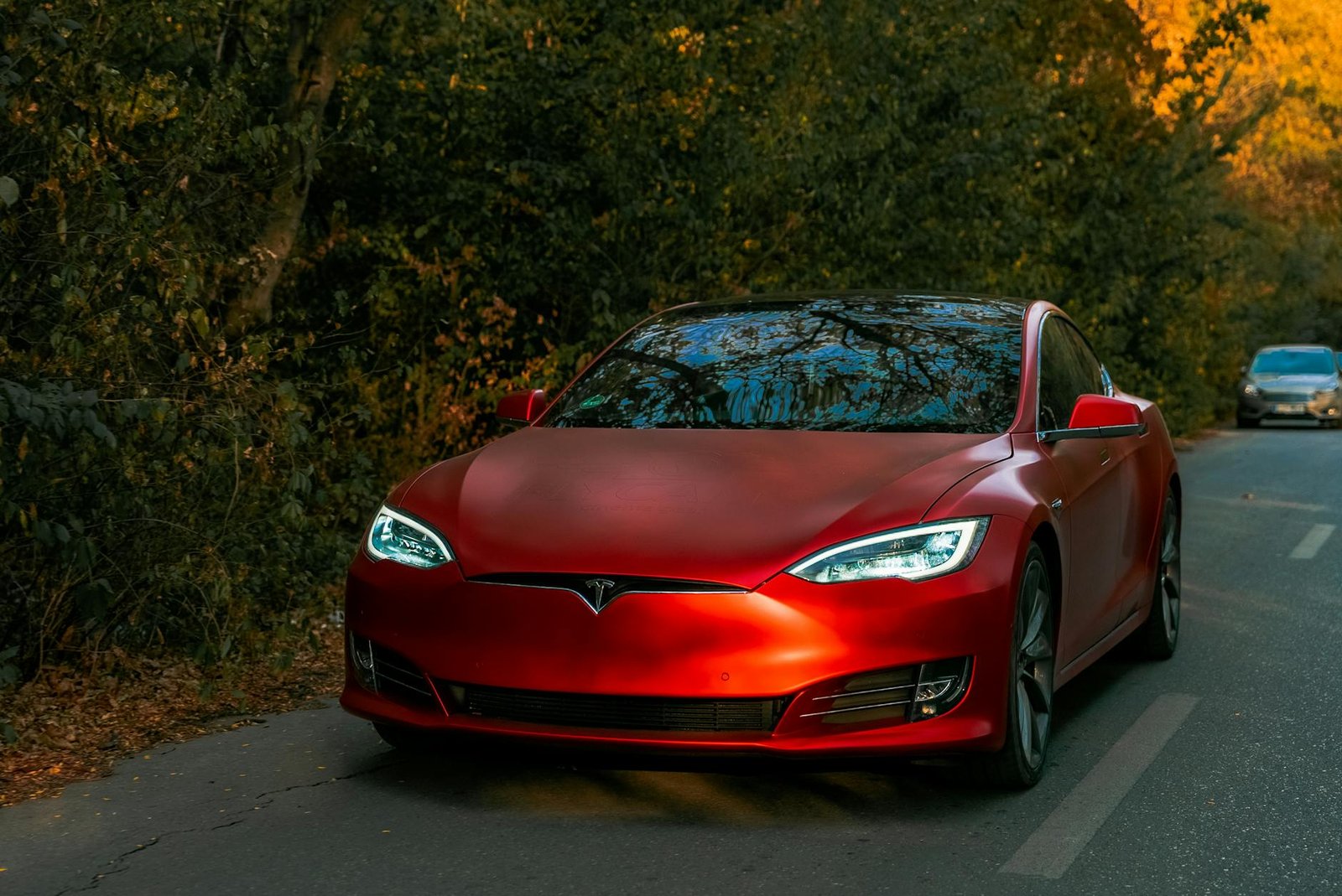 Sleek red electric car driving through a scenic forest road on an autumn day.
