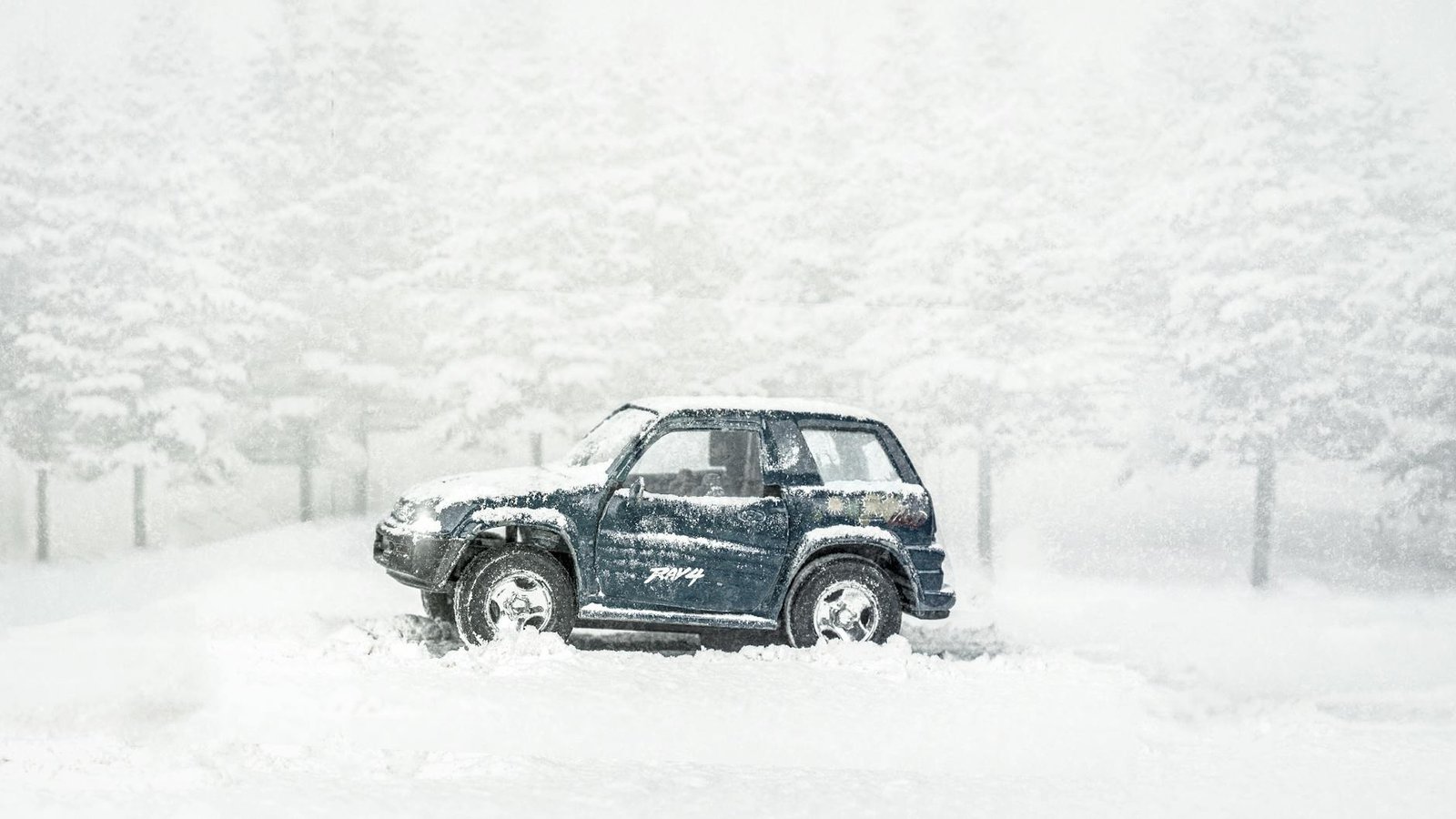 A Toyota RAV4 navigates through a heavy snowstorm and icy winter landscape.