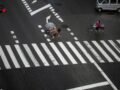 Cyclists navigate a rainy city crosswalk with umbrellas for protection.