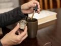 Close-up of hands using hemp extract oil with dropper into a cup indoors.
