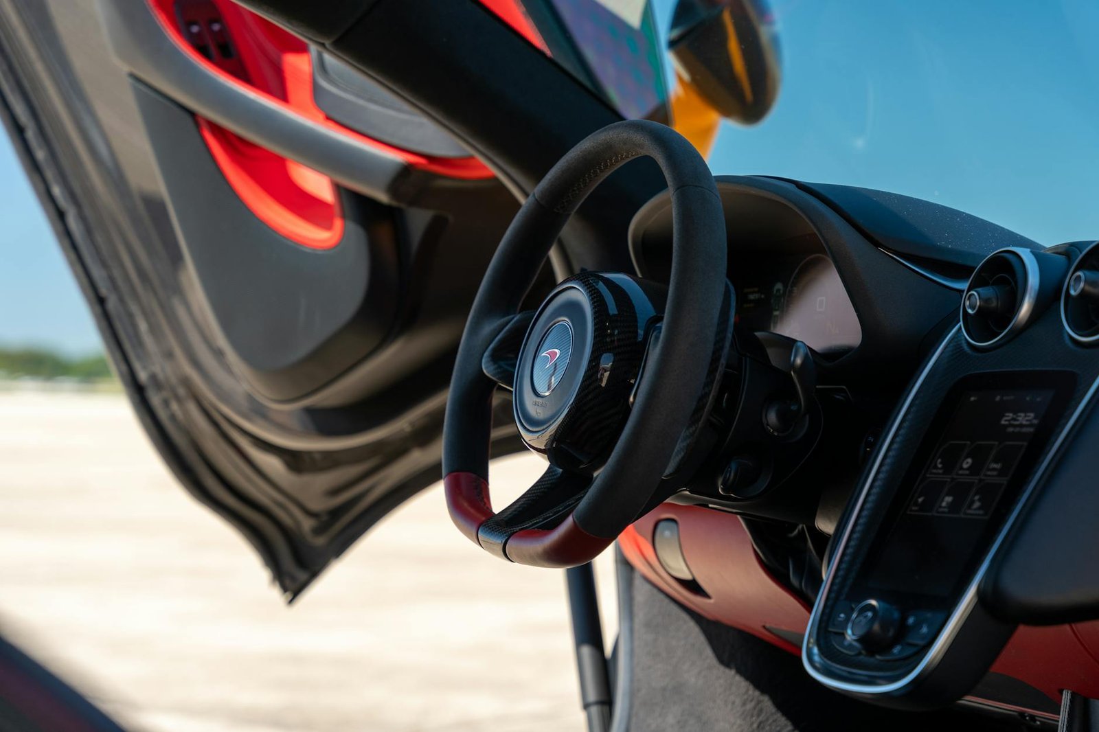 Close-up of a McLaren interior featuring a sleek steering wheel and open gullwing door, showcasing luxury design.