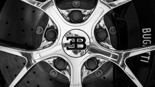 Black and white close-up shot of a Bugatti car rim showing intricate design and luxury branding.