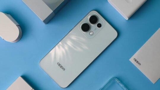 Flat lay of a sleek smartphone with accessories on a blue surface, featuring an elegant design.