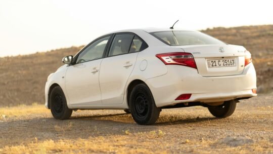 A white Toyota Vios parked in a desert landscape during daylight.