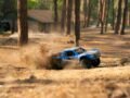 Blue remote control truck kicks up dirt on a wooded trail, showcasing dynamic motion.