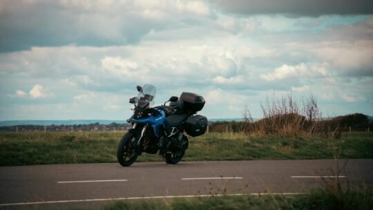 A blue motorcycle parked on a road in the English countryside under a cloudy sky.