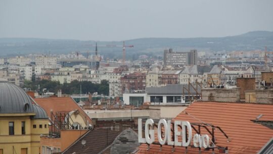 A cityscape above rooftops featuring an LG OLED sign against a distant urban backdrop.