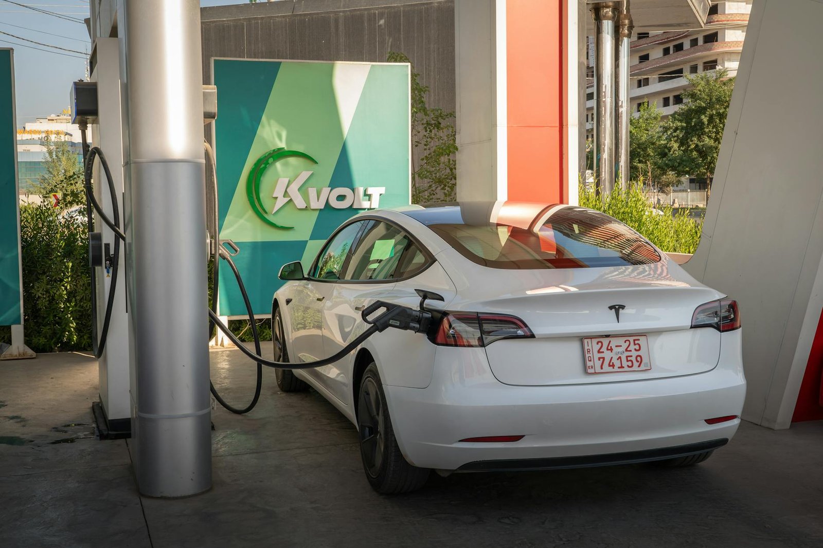 A white Tesla Model 3 charging at an outdoor electric vehicle station with Kvolt branding.