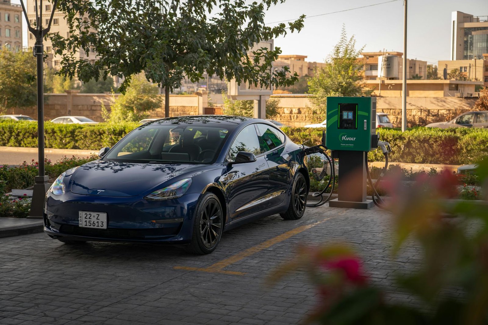 Tesla Model 3 charging at an urban electric vehicle station during daytime.
