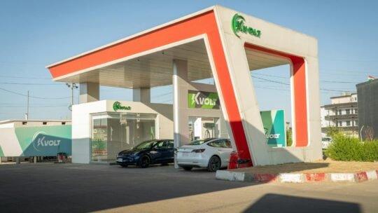 A futuristic electric vehicle charging station featuring Tesla cars under a bright blue sky.