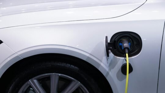 A white electric car is plugged in for charging, close-up view of the charging port.