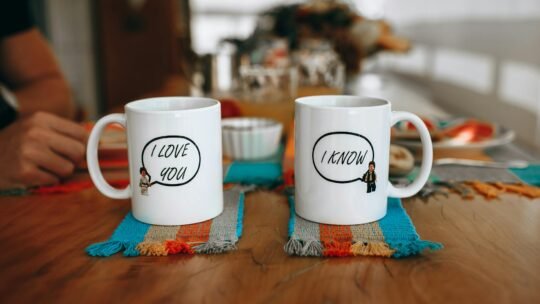 Two mugs with playful text on a table showcasing a cozy indoor setting.
