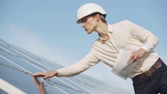A solar technician in a hard hat inspecting photovoltaic panels under clear skies.