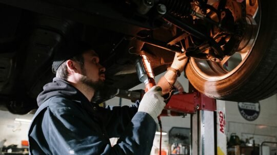 Mechanic examining car's undercarriage at a garage, focusing on vehicle maintenance.