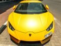 Front view of a parked yellow Lamborghini Aventador on a sunny Dubai street.