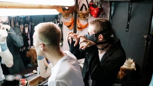 Diverse performers prepare with makeup and costumes in a vibrant dressing room.