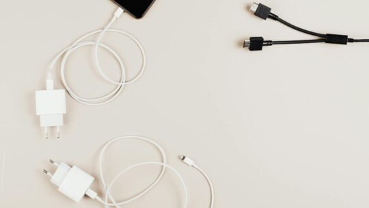 Flat lay of mobile devices with chargers and cables on a neutral background.