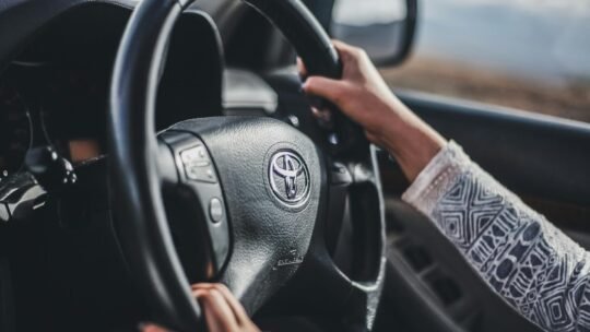 Hands gripping the wheel of a moving car, showcasing driving focus and control.