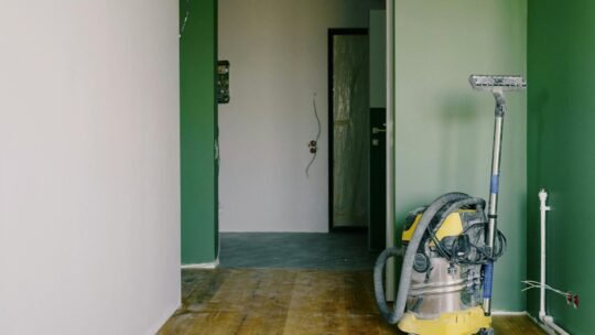 Industrial vacuum cleaner placed on dirty parquet in room with green walls and doorway in spacious apartment during repair works