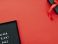 Top view of a Black Friday sale sign and gift box on a vibrant red background.
