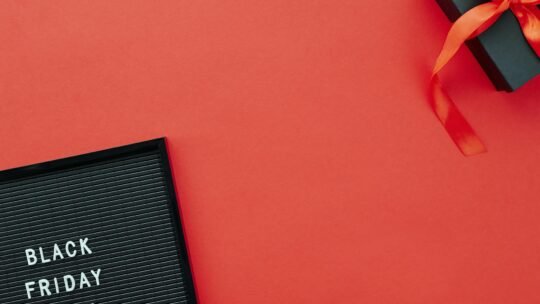 Top view of a Black Friday sale sign and gift box on a vibrant red background.