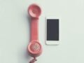 Comparison of a vintage pink telephone receiver and a modern smartphone on a simple backdrop.