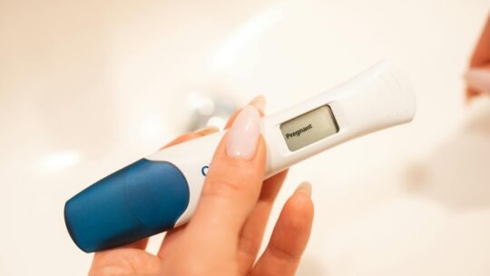 Close-up view of a positive digital pregnancy test held by a woman with manicured nails.
