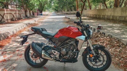 A red motorcycle parked on a tree-lined road in daylight, creating a vibrant street scene.