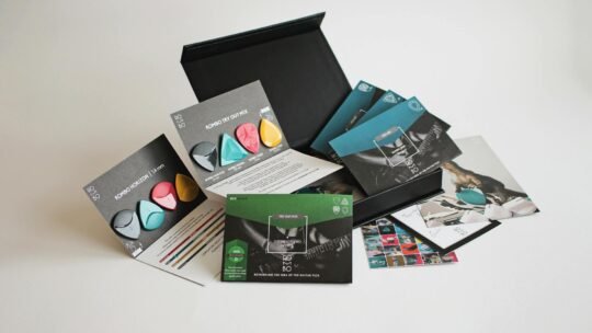 A variety pack of colorful guitar picks with packaging and promotional materials.