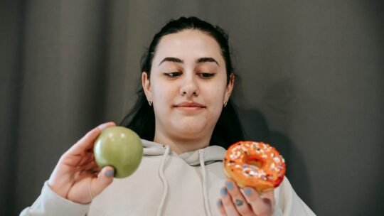 A young woman ponders a healthy apple versus a tempting donut. Lifestyle choice dilemma.